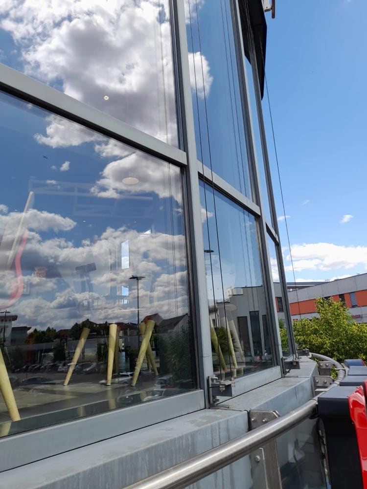Gebäude mit Glasfassade, reflektierenden Wolken und Himmel, moderne Architektur, sonniger Tag.