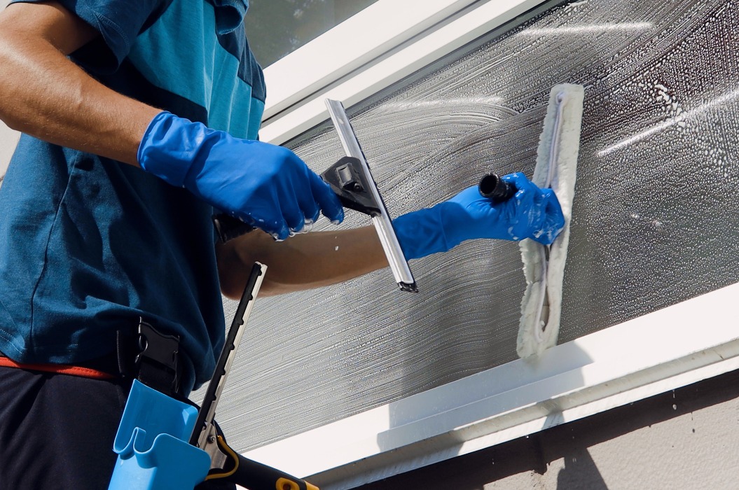 Männlicher professioneller Reinigungsdienstmitarbeiter im Overall reinigt die Fenster und Schaufenster eines Geschäfts mit einer speziellen Ausrüstung